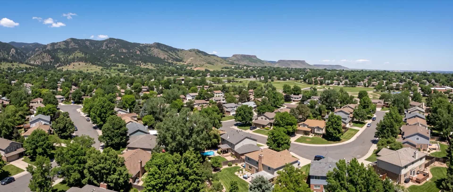 Illustrative representation of established suburban rooftops and mature shade trees in Arvada, Colorado, with the Front Range foothills to the northwest