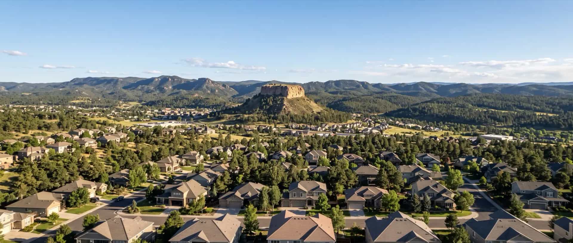 Illustrative representation of rooftops among ponderosa pines in Castle Rock, Colorado, with the town's flat-topped sandstone butte behind