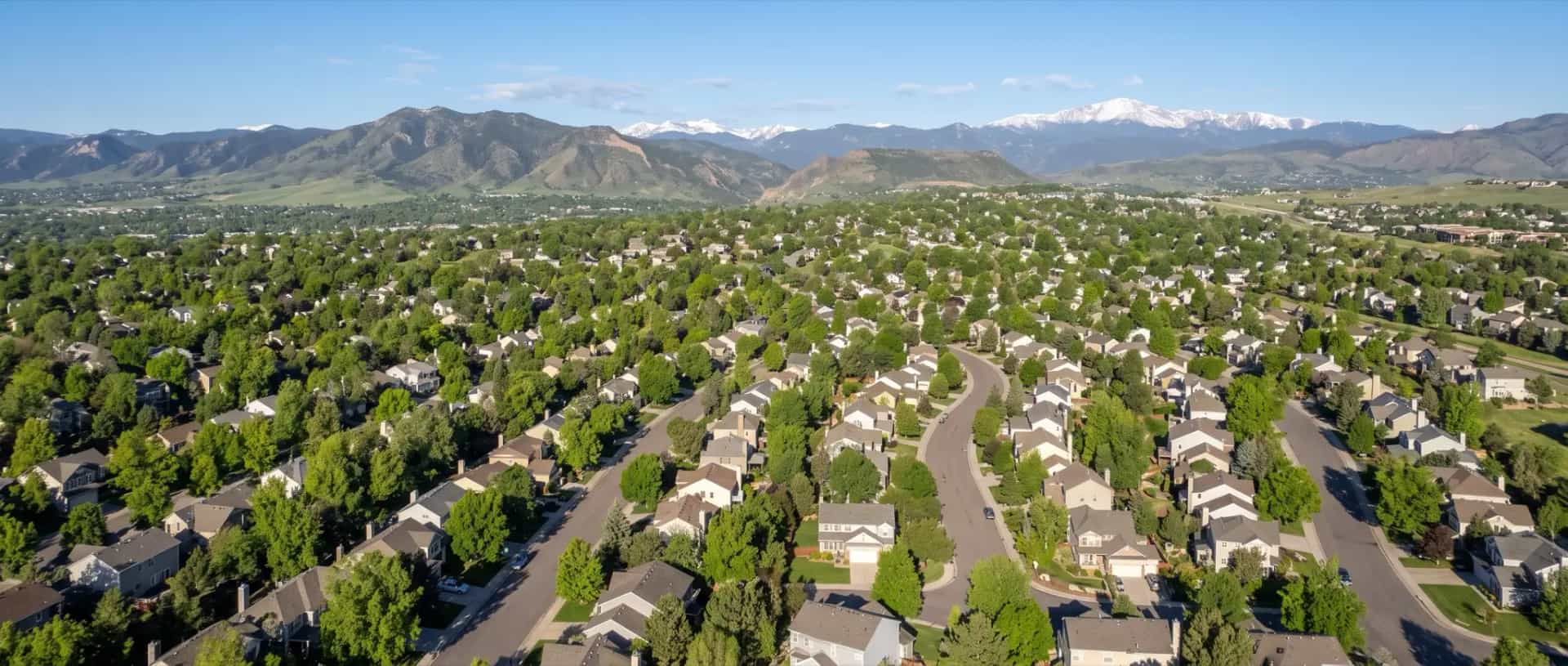 Illustrative representation of established suburban rooftops and mature tree canopy in Centennial, Colorado, with the Front Range foothills beyond