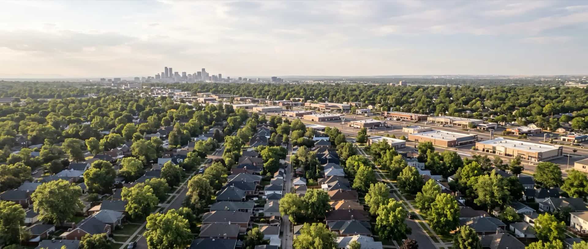 Illustrative representation of compact older rooftops under mature trees in Englewood, Colorado, with the Denver skyline beyond