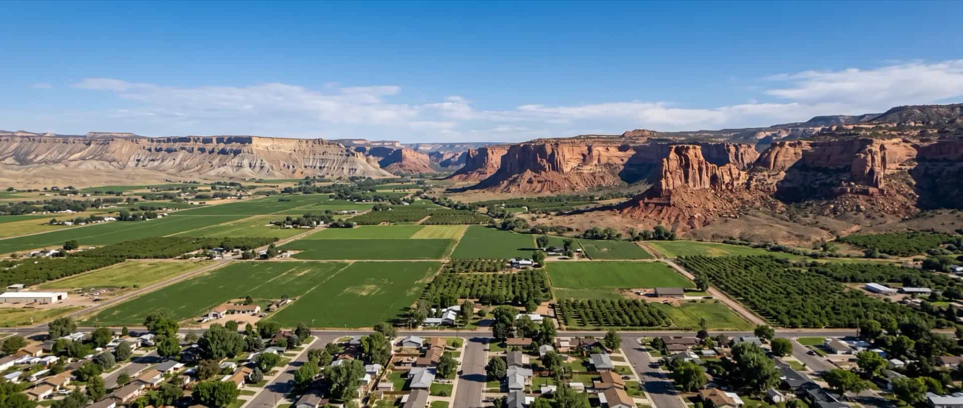 Illustrative representation of rooftops and irrigated farm plots in Fruita, Colorado beneath the red sandstone cliffs of the Grand Valley