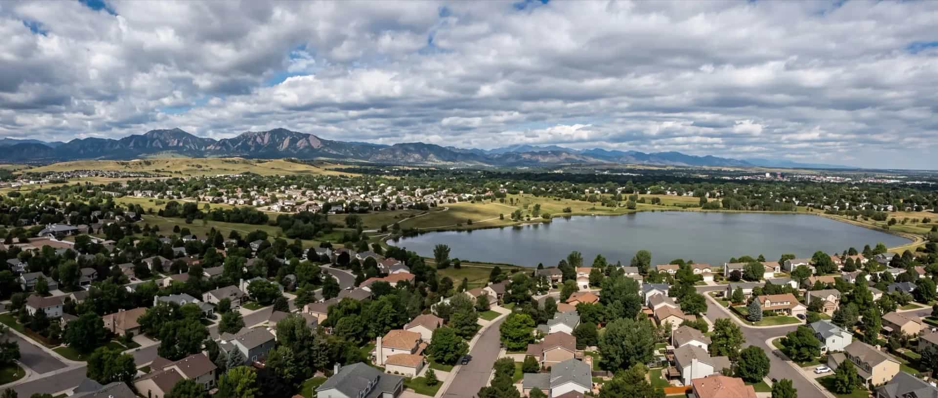 Illustrative representation of suburban rooftops around open space and a reservoir in Westminster, Colorado under broken cloud