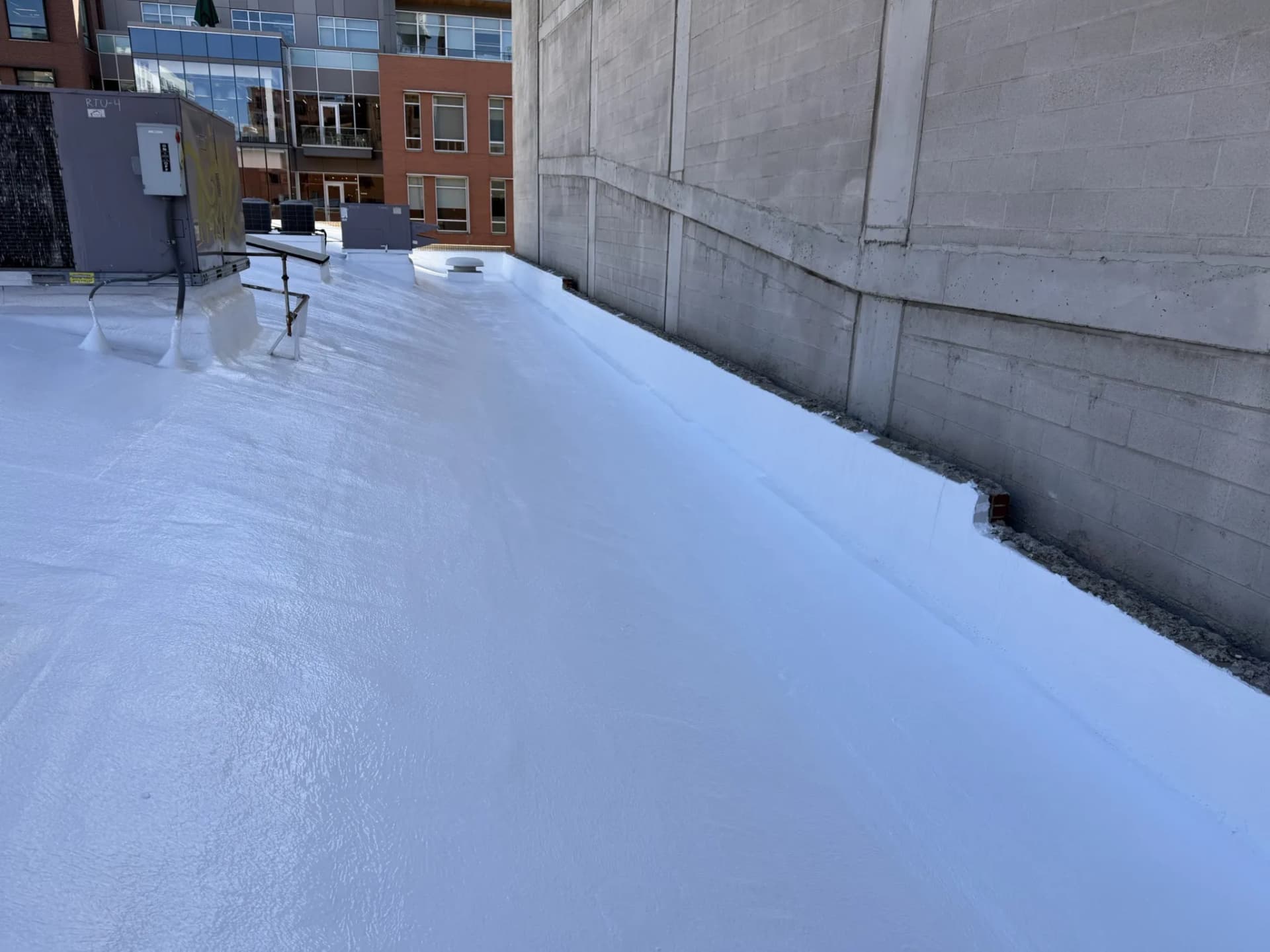 Finished white American WeatherStar Ure-A-Sil roof coating carried up the parapet wall on a commercial building in downtown Denver, Colorado