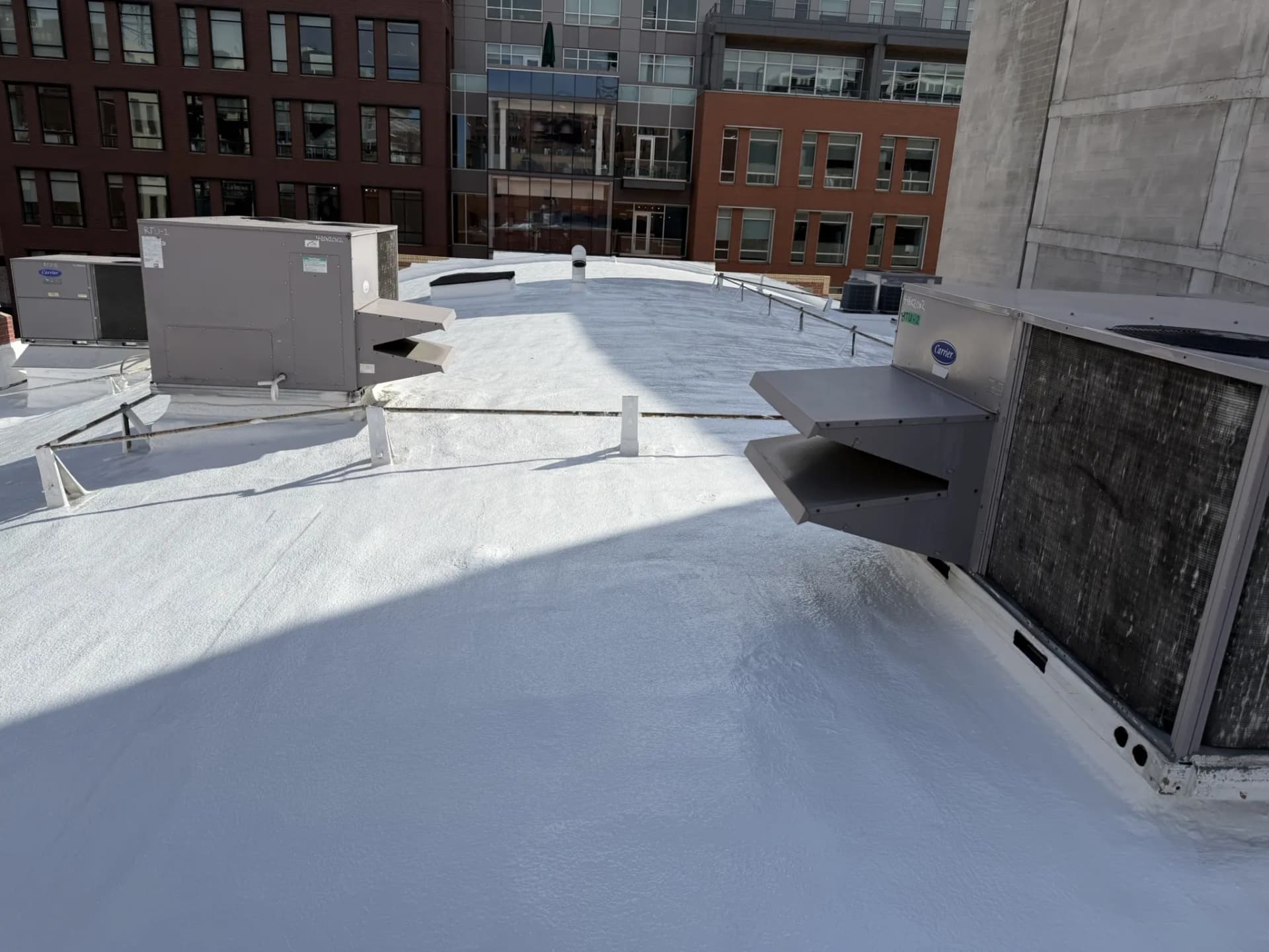 Completed white silicone roof coating around rooftop HVAC unit curbs on a commercial building in downtown Denver, Colorado