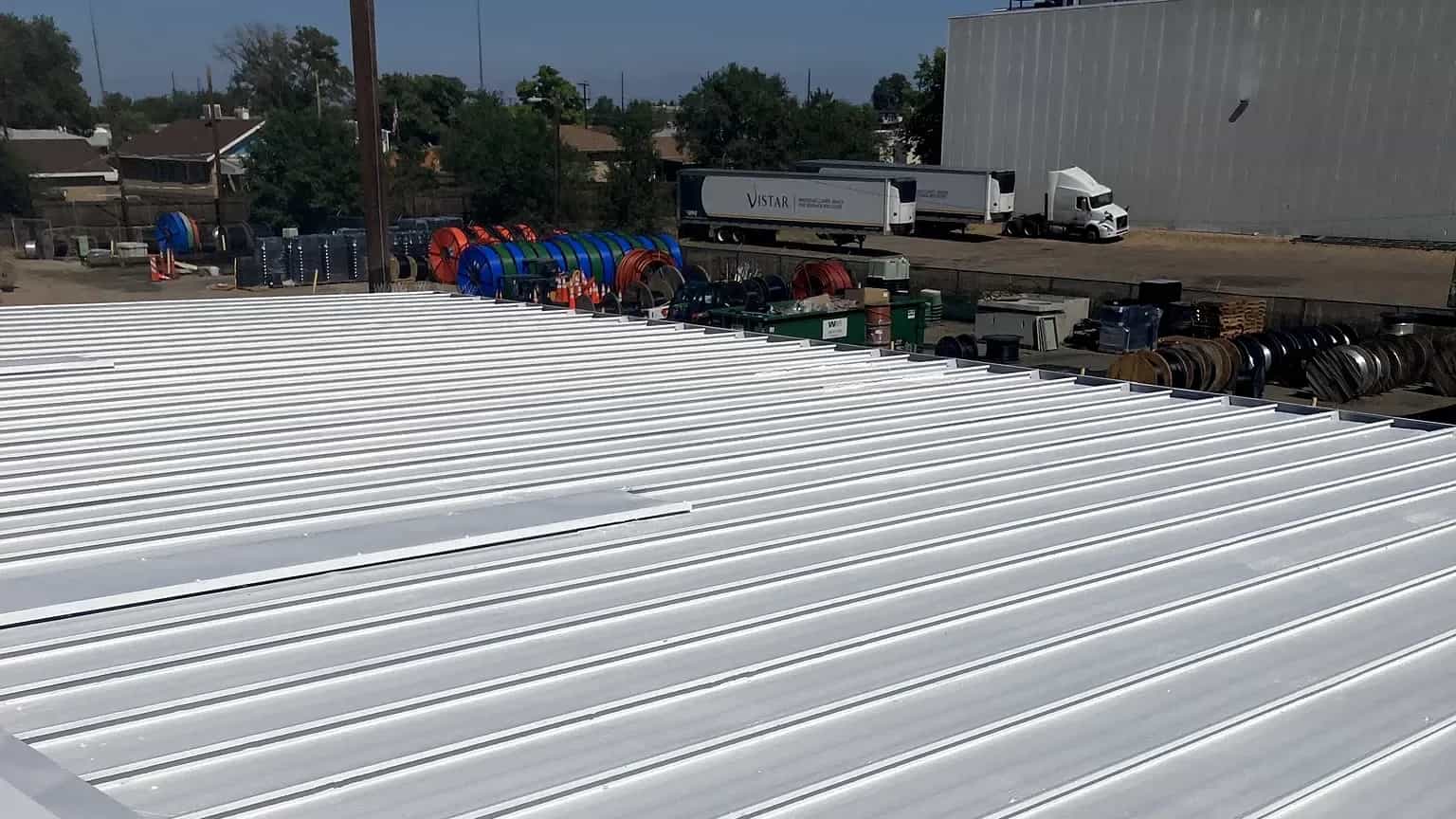 Commercial metal roof in Denver, Colorado finished in a bright white American WeatherStar reflective coating, industrial backdrop behind it