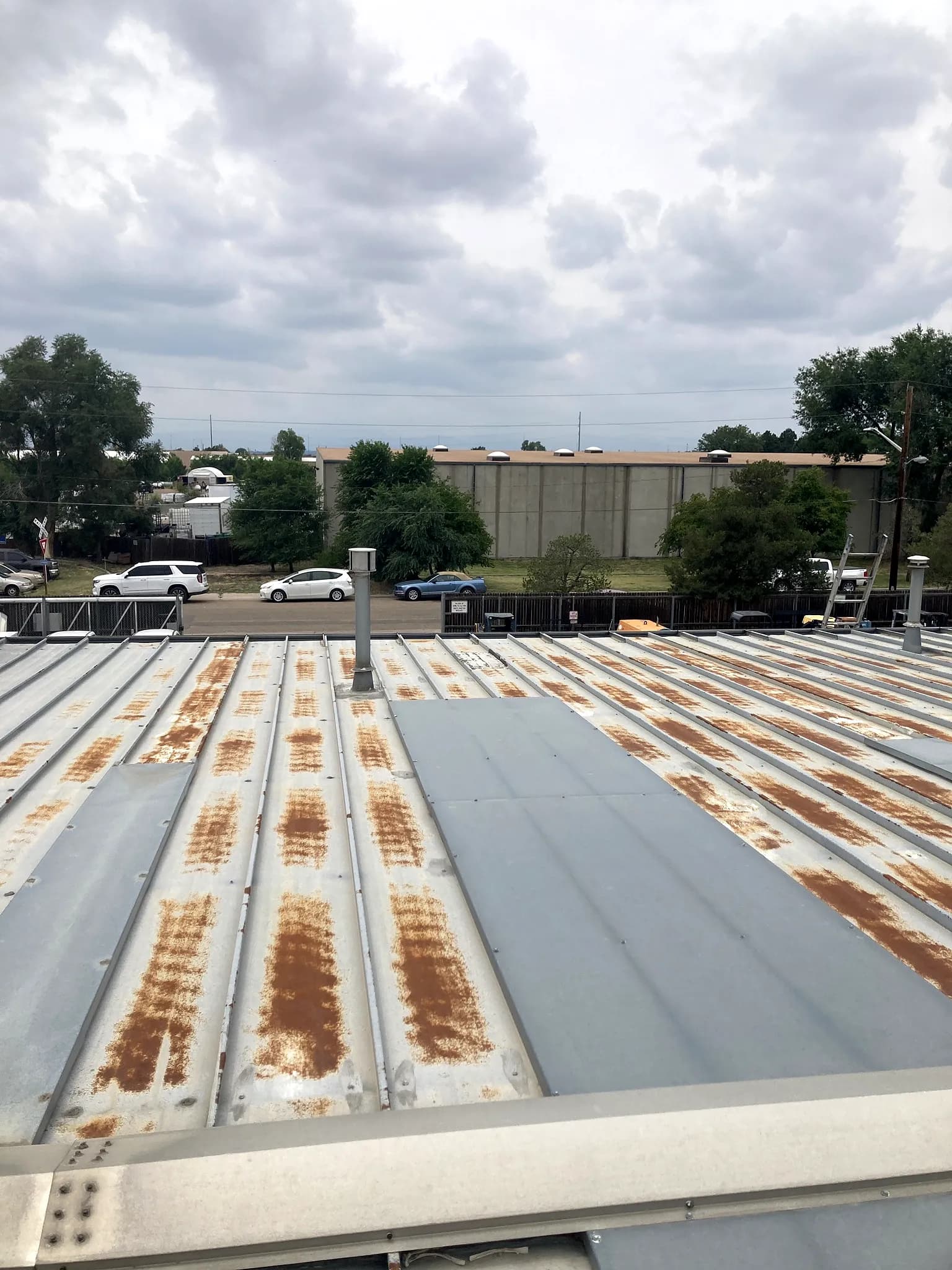 Close-up of corroded seams and fasteners on an aging exposed-fastener metal commercial roof in Denver, Colorado