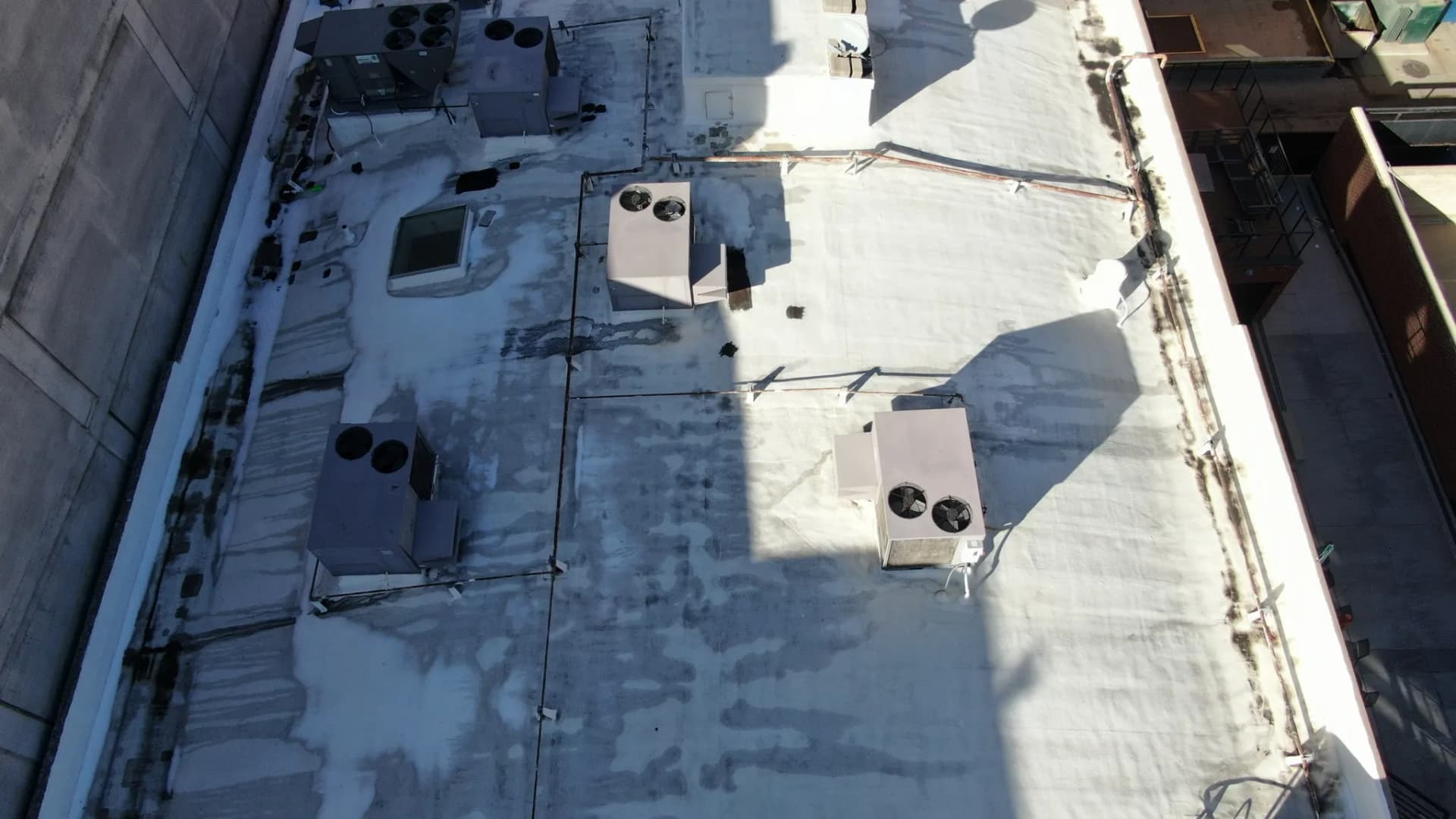 Aerial view of a worn, streaked roof coating with dark ponding stains on a commercial building in downtown Denver, Colorado before restoration