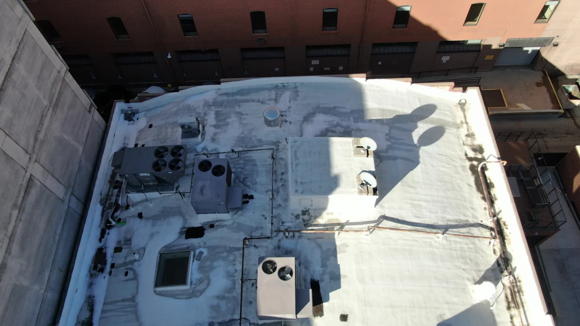 Wider aerial view of an aging low-slope commercial roof coating in downtown Denver, Colorado, hemmed in by neighboring buildings