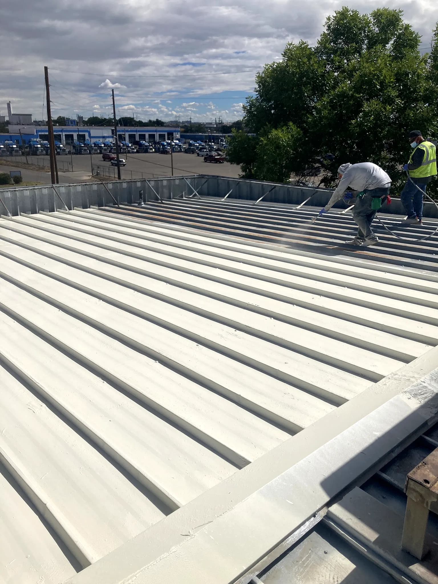 Crew spray-applying the American WeatherStar Met-a-Gard+ coating across a commercial metal roof in Denver, Colorado