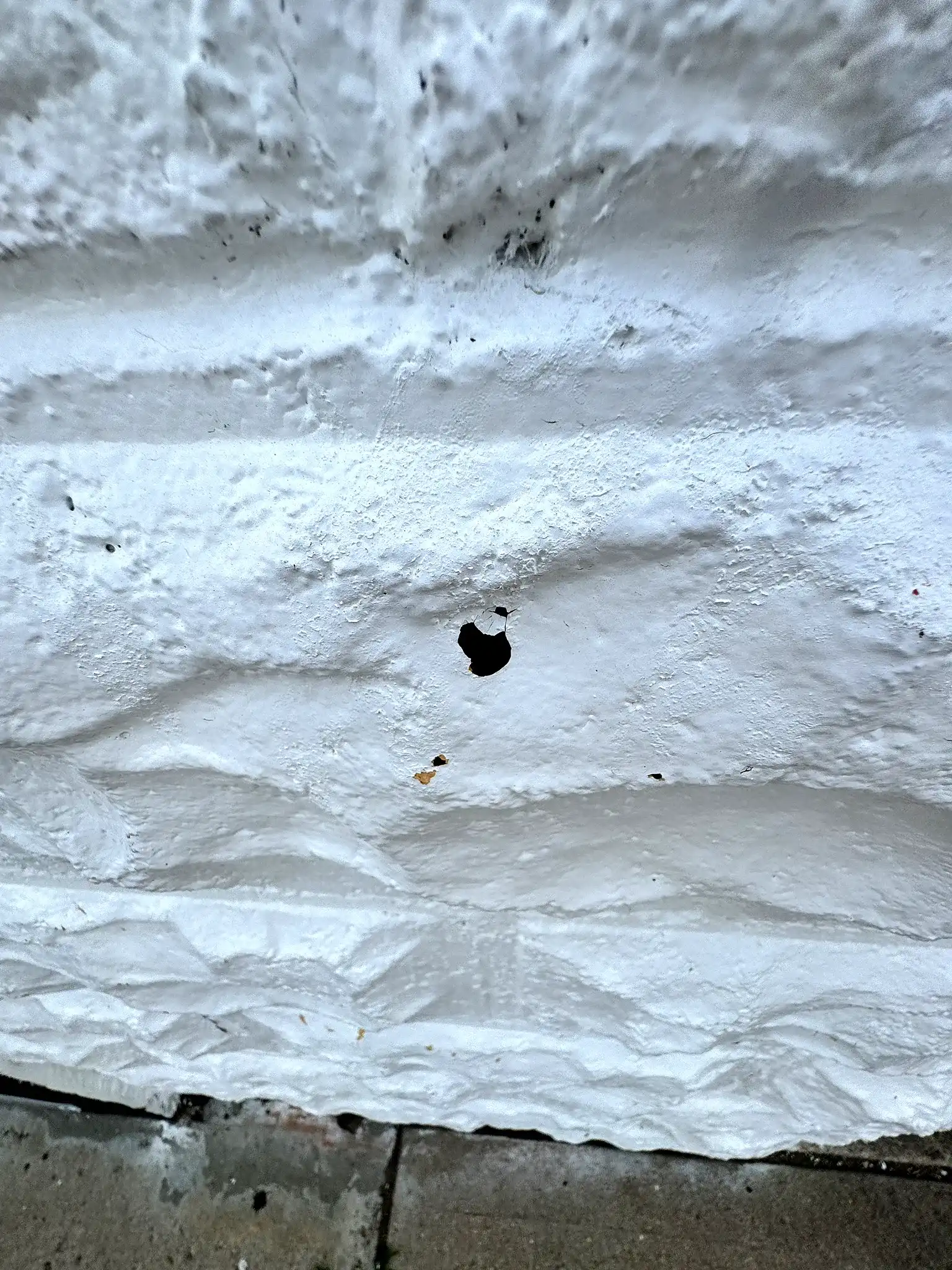Close-up of a hail puncture through the white-coated parapet coping on a commercial building in Greeley, Colorado