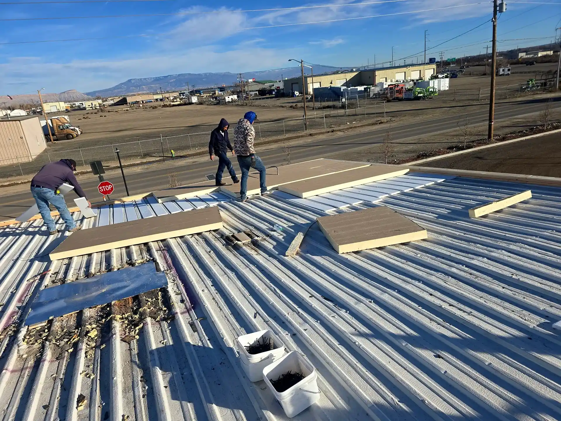 Rigid polyiso insulation boards being installed over an existing metal roof during a commercial TPO membrane recover in Grand Junction