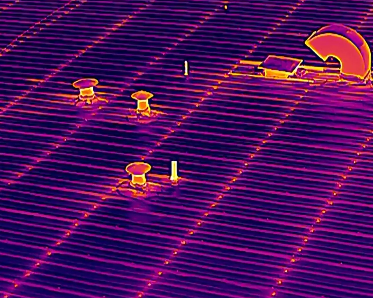 Drone thermal infrared scan of a ribbed commercial metal roof in Grand Junction, Colorado, showing warm hot spots at seams and fasteners where water is entering
