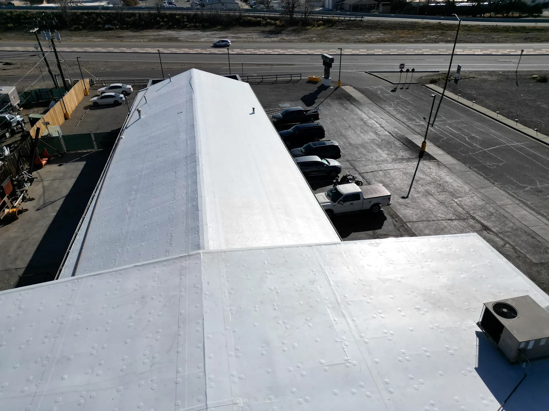 Aerial view of a finished white TPO membrane roof showing the pattern of induction-welded fastening plates on a commercial building along Highway 50 in Grand Junction, Colorado