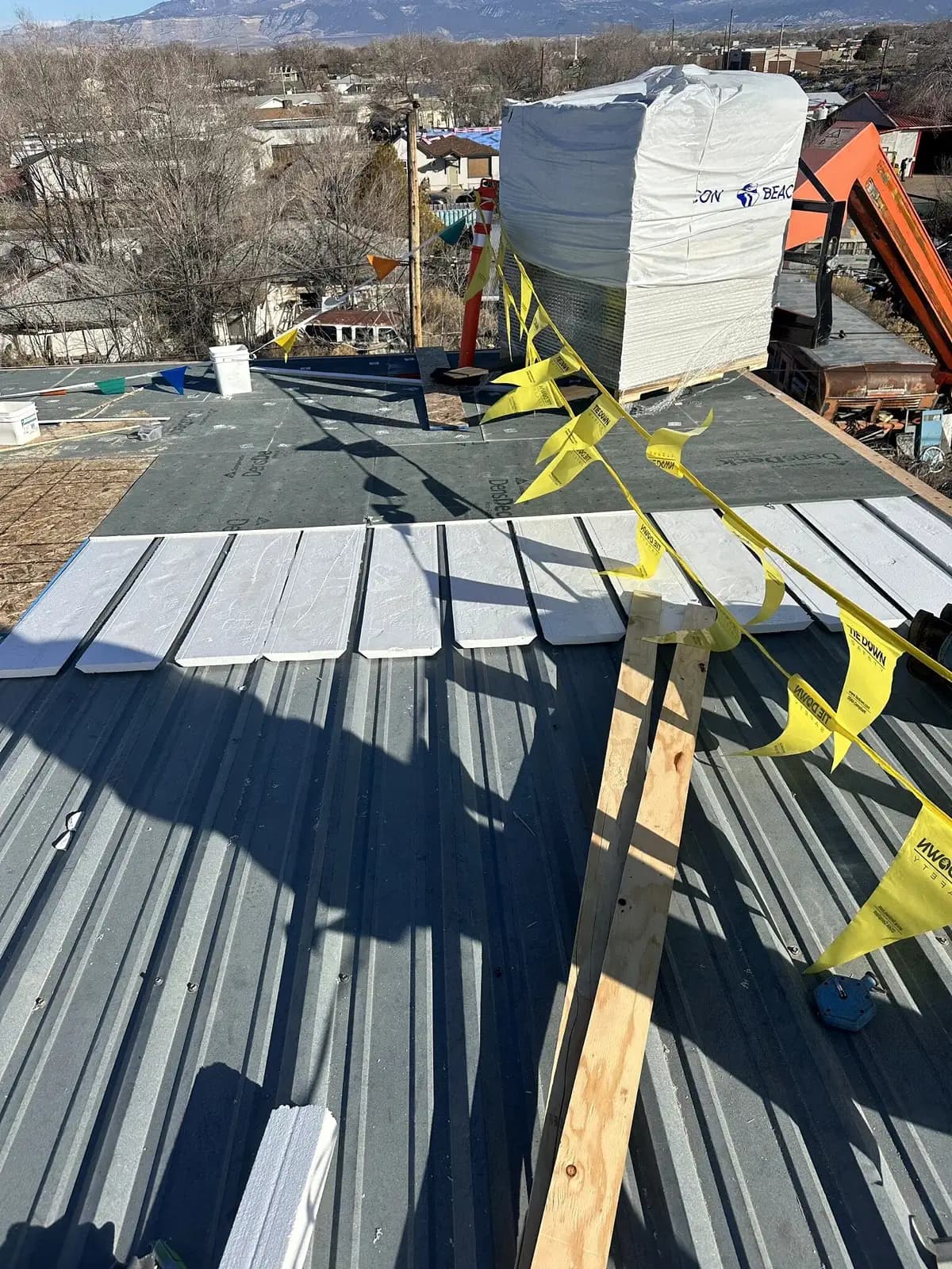 Rigid polyiso insulation and DensDeck cover board being installed over an existing ribbed metal roof during a recover in Grand Junction, Colorado, with the Grand Mesa in the background