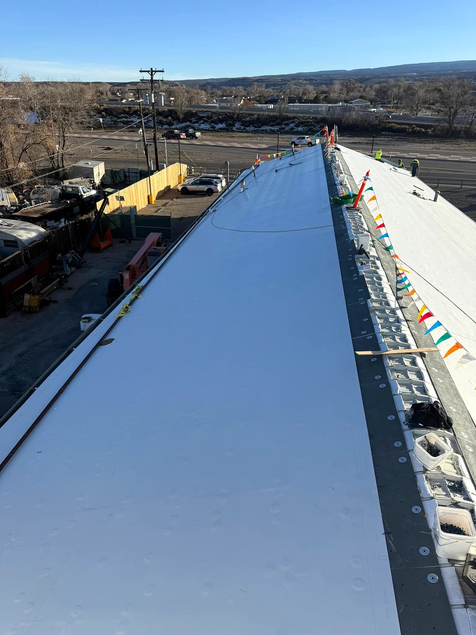 White 60-mil TPO membrane dried in on a low-slope commercial roof with round induction-weld fastening plates visible along the edge in Grand Junction, Colorado