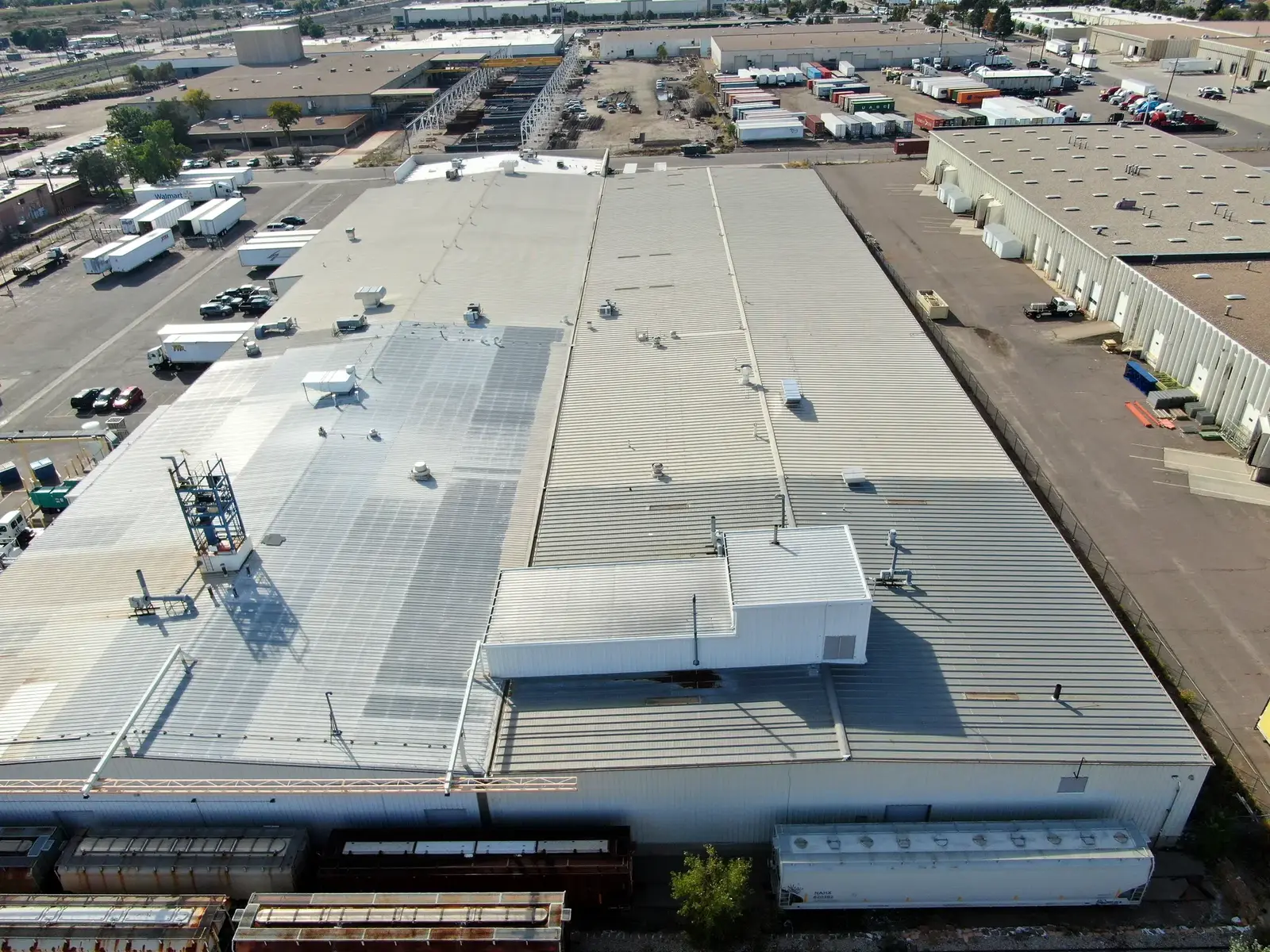 Drone view of a large ribbed metal roof on an industrial chemical facility in Denver, Colorado, with the penthouse and rail cars along the east edge
