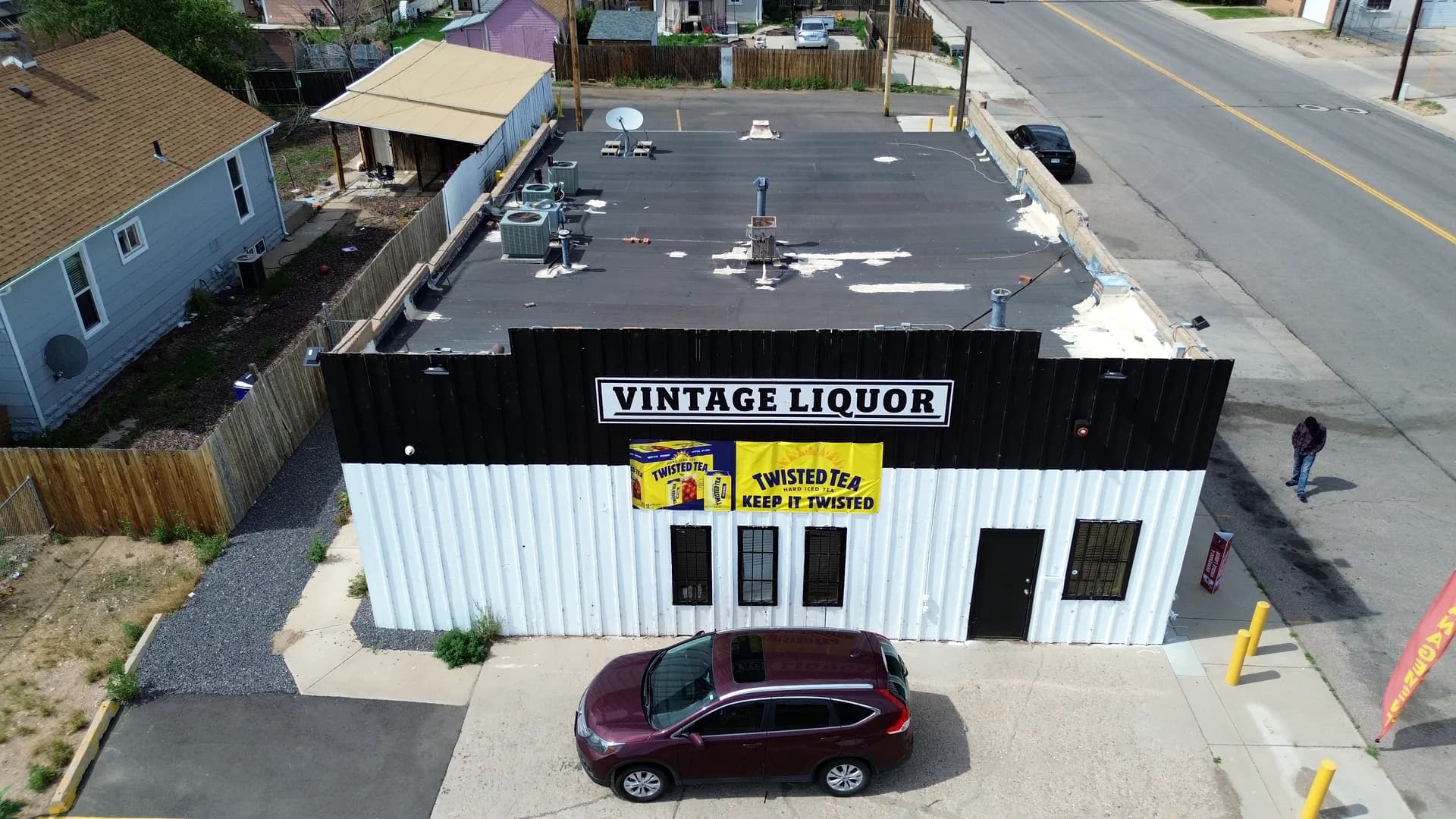 Aerial view of the aged, patch-repaired dark low-slope roof on the Vintage Liquor building in Greeley, Colorado before replacement