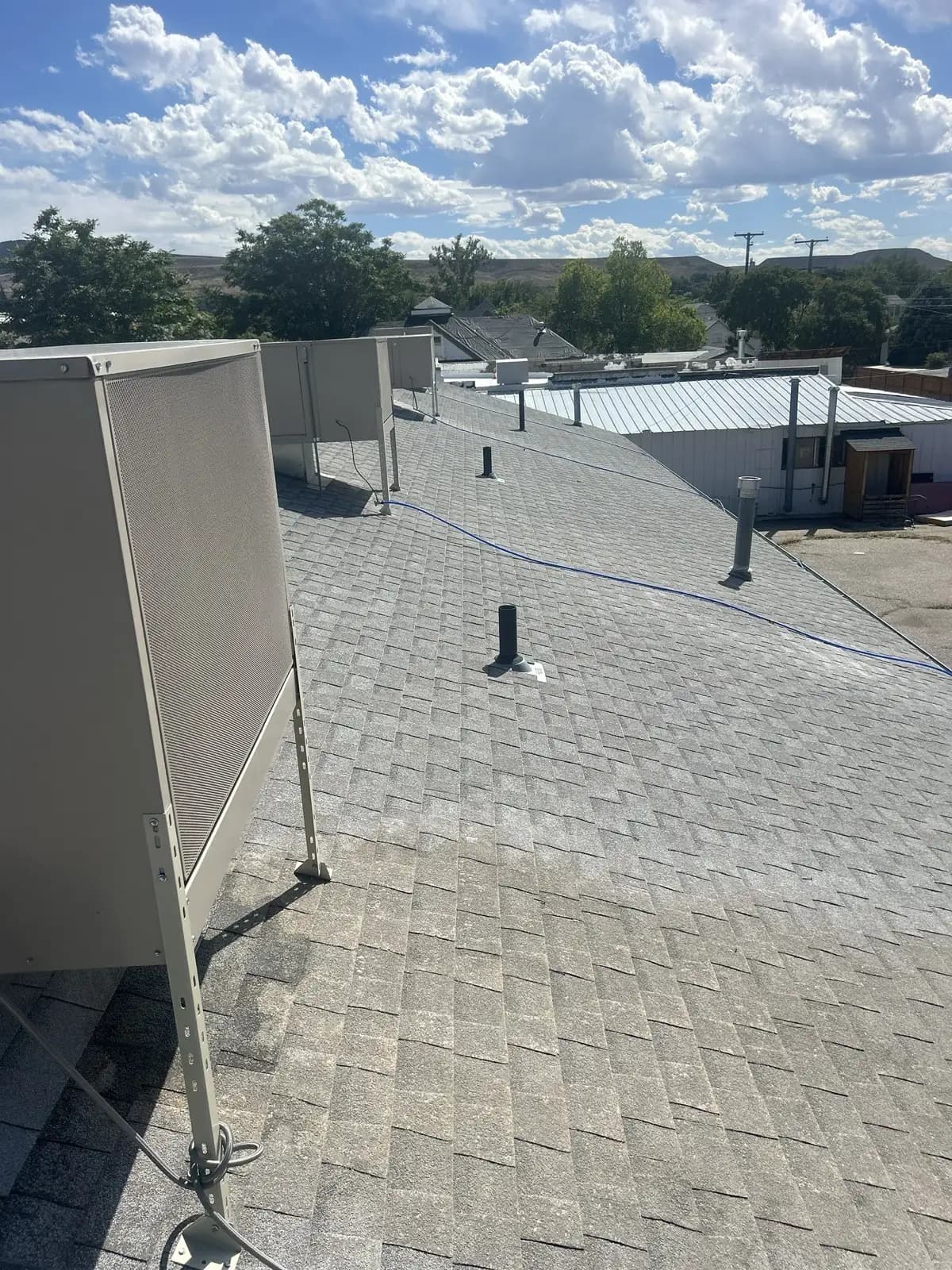 Asphalt shingle roof on a commercial building in Palisade, Colorado with rooftop mechanical units and screens, the Book Cliffs visible behind