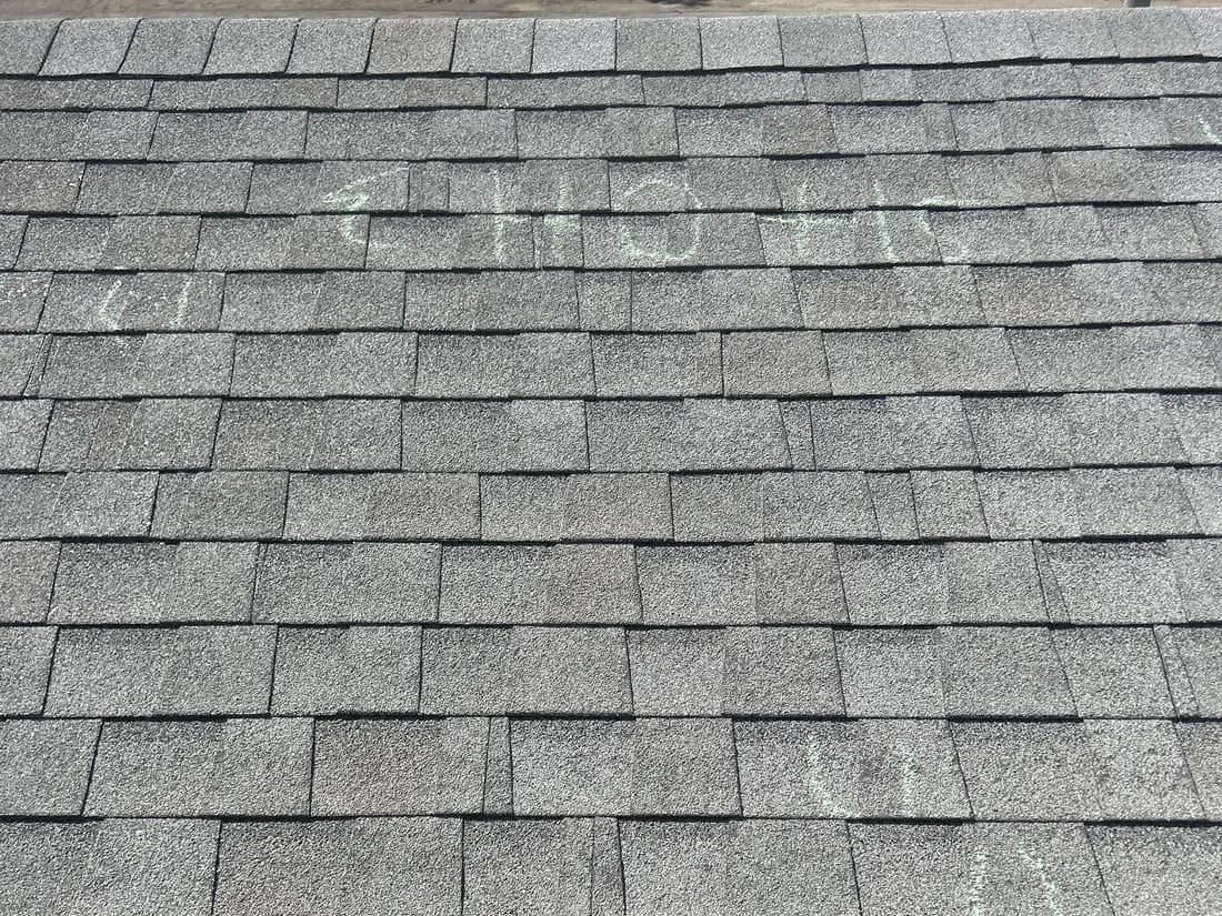 A chalked test square on the asphalt shingle roof of a commercial building in Palisade, Colorado, with the hail impact count written on the shingles