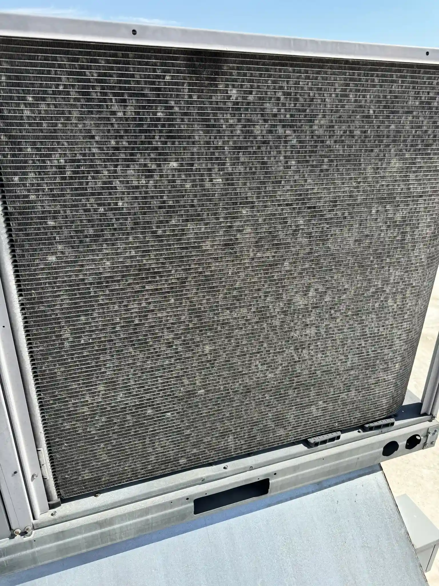Close-up of a hail-damaged micro-channel condenser coil on a rooftop HVAC unit at a commercial building in Denver, Colorado