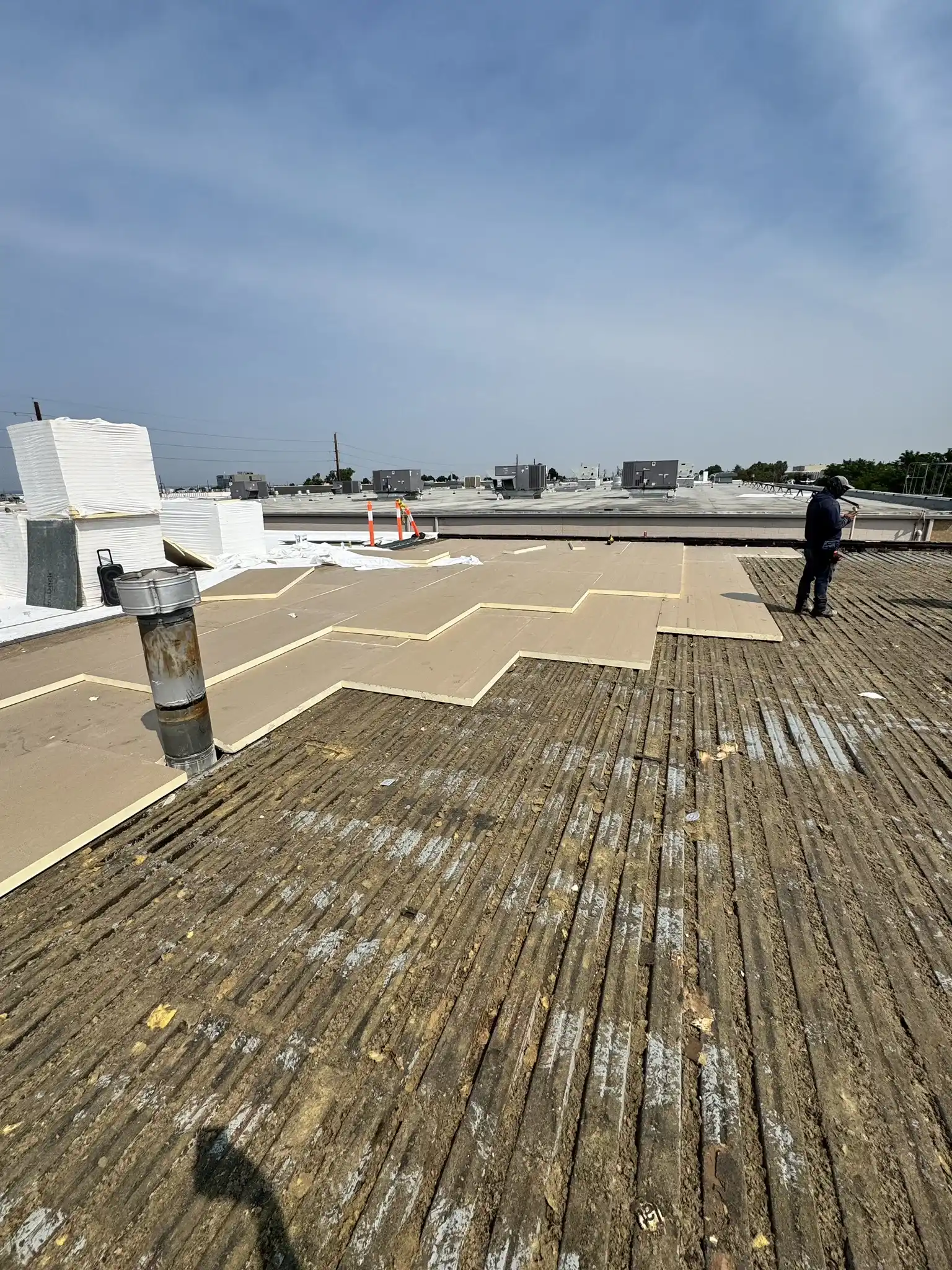 Tear-off in progress showing the original corrugated metal roof deck with new polyiso insulation being laid over it on a Denver commercial roof