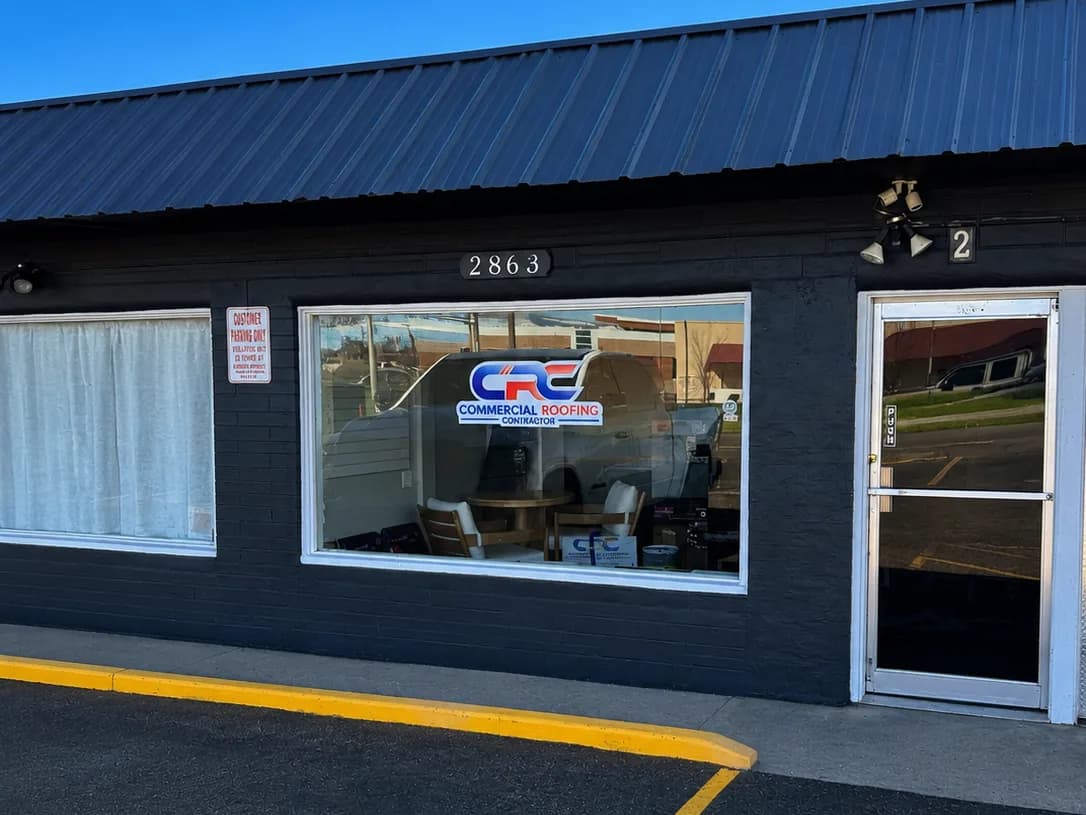 The Commercial Roofing Contractor Grand Junction office on North Avenue seen from the parking lot, a dark brick storefront with a metal awning and the CRC logo in the window