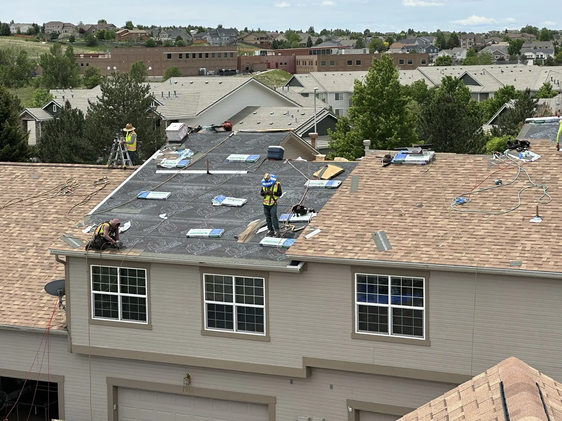 A CRC crew installing RhinoRoof synthetic underlayment on a Colorado Springs condominium roof, with new shingle bundles staged along the ridge and the community behind