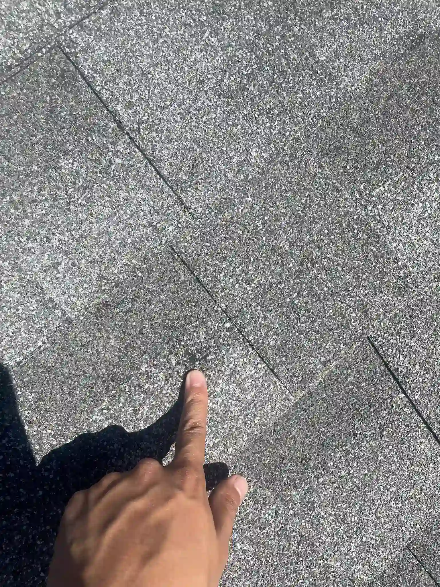 Hand pointing to a hail-bruised shingle during a roof inspection on an Aurora, Colorado home