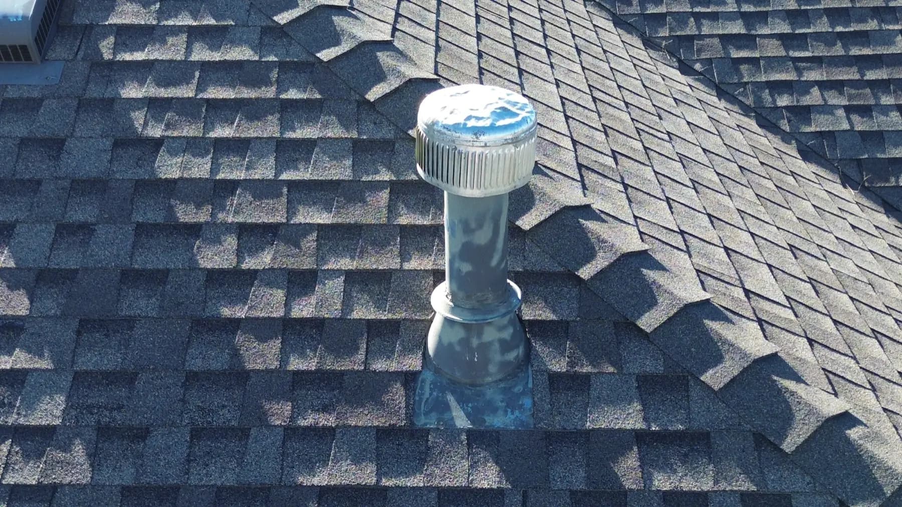 Hail-dented metal roof vent cap surrounded by weathered, granule-worn asphalt shingles on a home in Castle Pines, Colorado