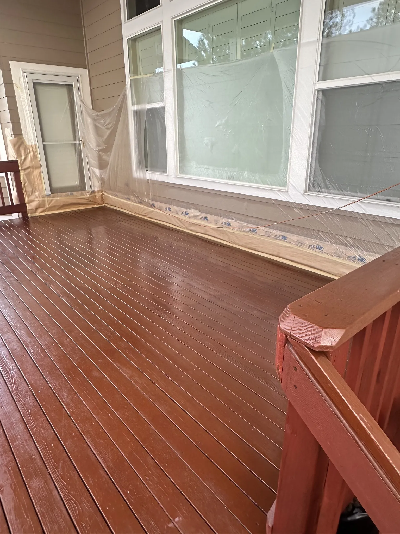 Freshly re-stained wood deck on a Castle Pines, Colorado, home in rich red-brown, with windows and siding masked off in plastic for exterior painting