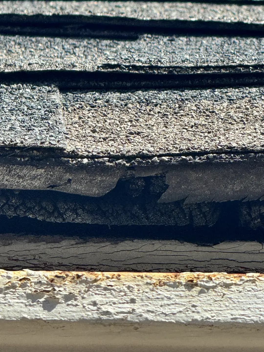 Close-up of stacked asphalt shingle layers and a rusted drip edge at the roof edge of an older building in Denver, Colorado