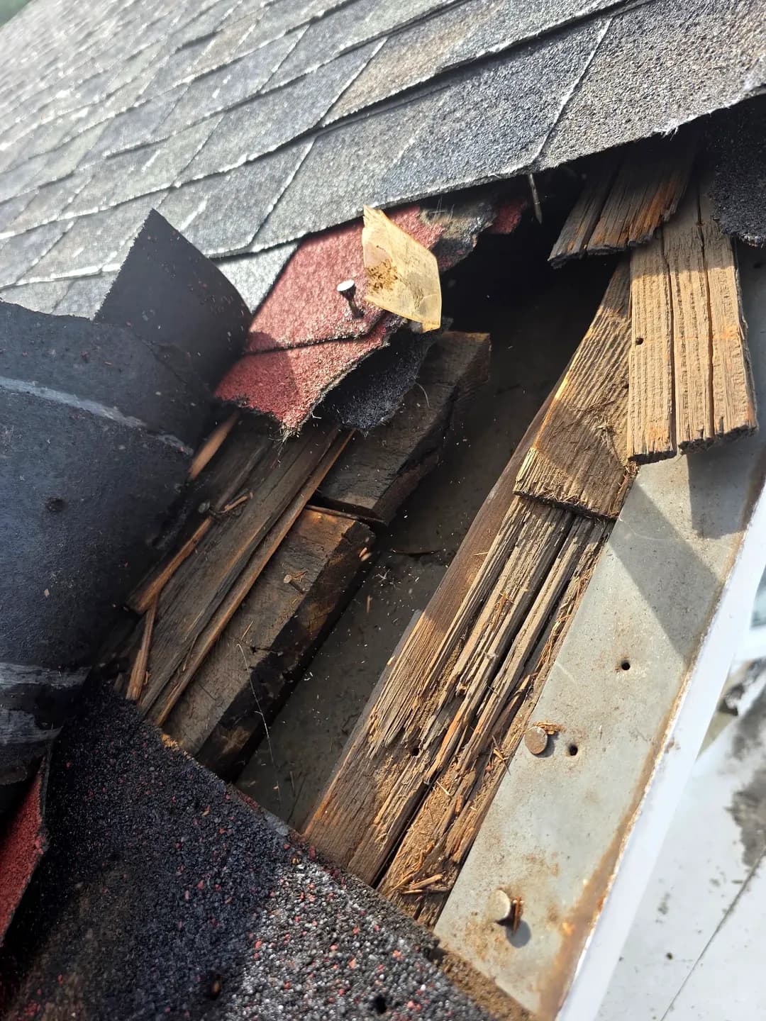 Deteriorated wood shakes and split decking boards exposed at the eave of an older Denver, Colorado, roof, with a gap open to the attic