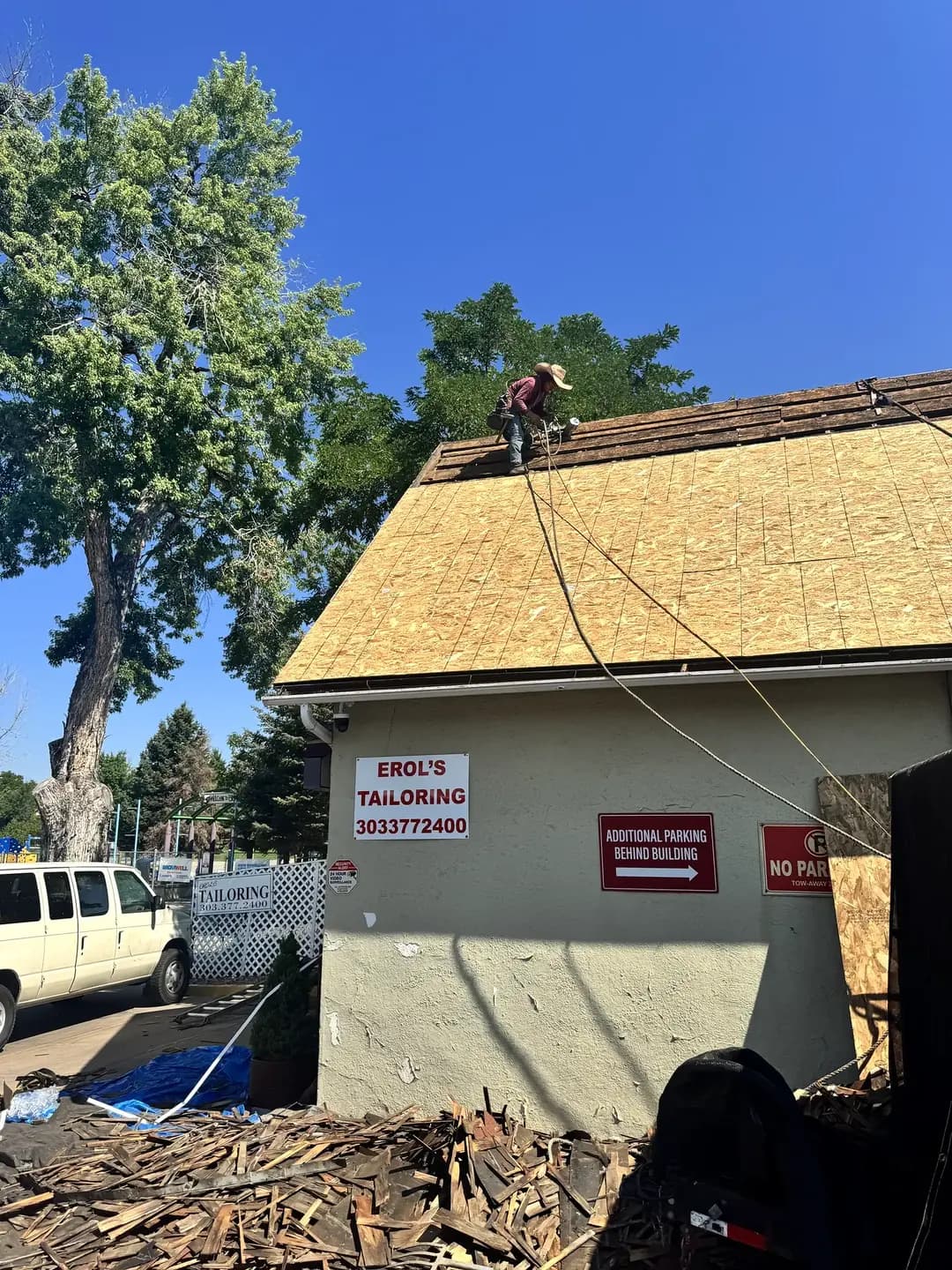 Completed new roof decking on Erol's Tailoring in Denver, Colorado, with a large pile of removed wood shakes stacked in the parking lot below