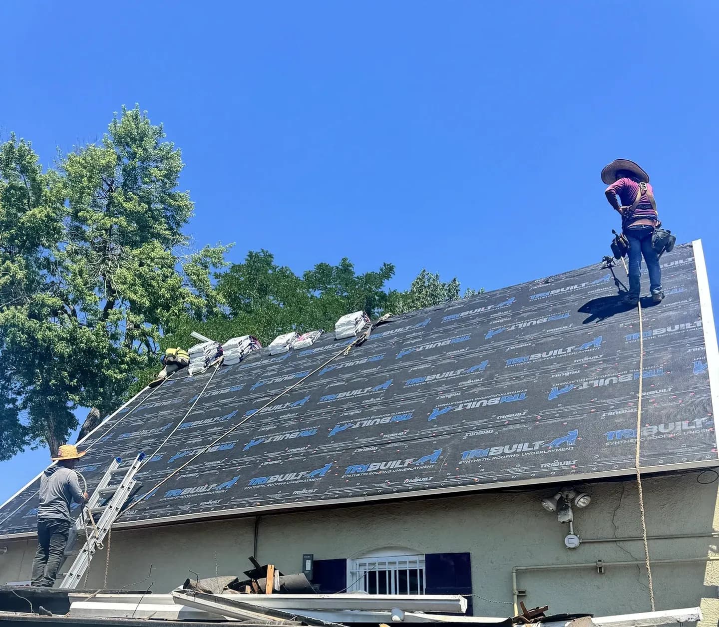 Synthetic underlayment installed over new roof decking on a steep roof in Denver, Colorado, with Class 4 shingle bundles staged along the slope