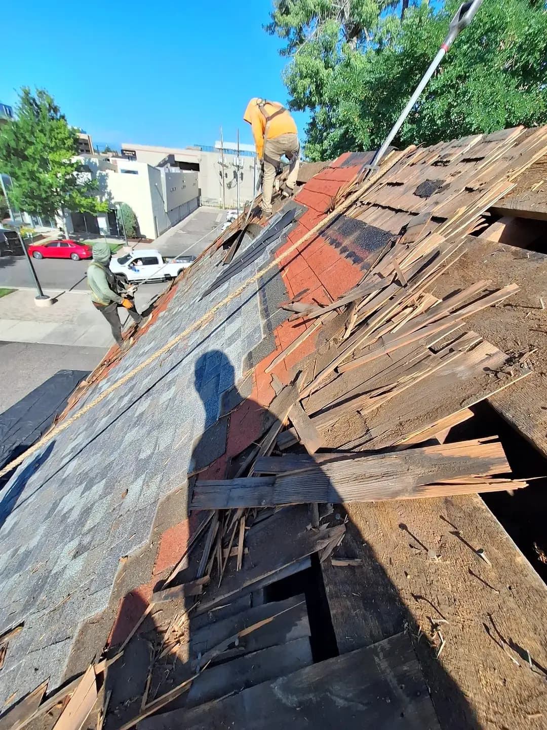 Roof tear-off in progress in Denver, Colorado, showing grey asphalt shingles over a red asphalt layer over the original wood shakes