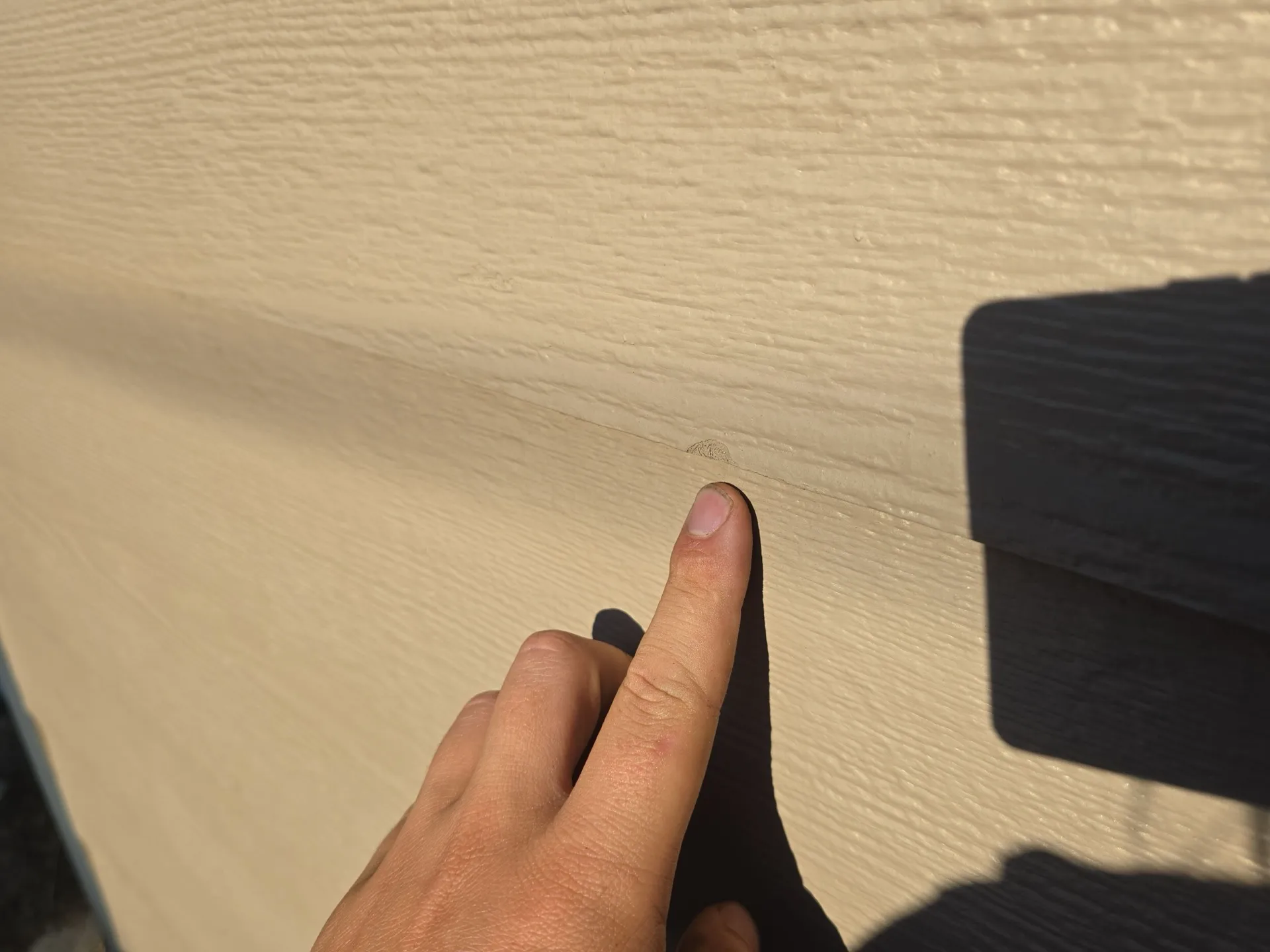 Gloved hand pointing to a hail dent in fiber cement lap siding on a home in Denver, Colorado, documented as collateral storm damage