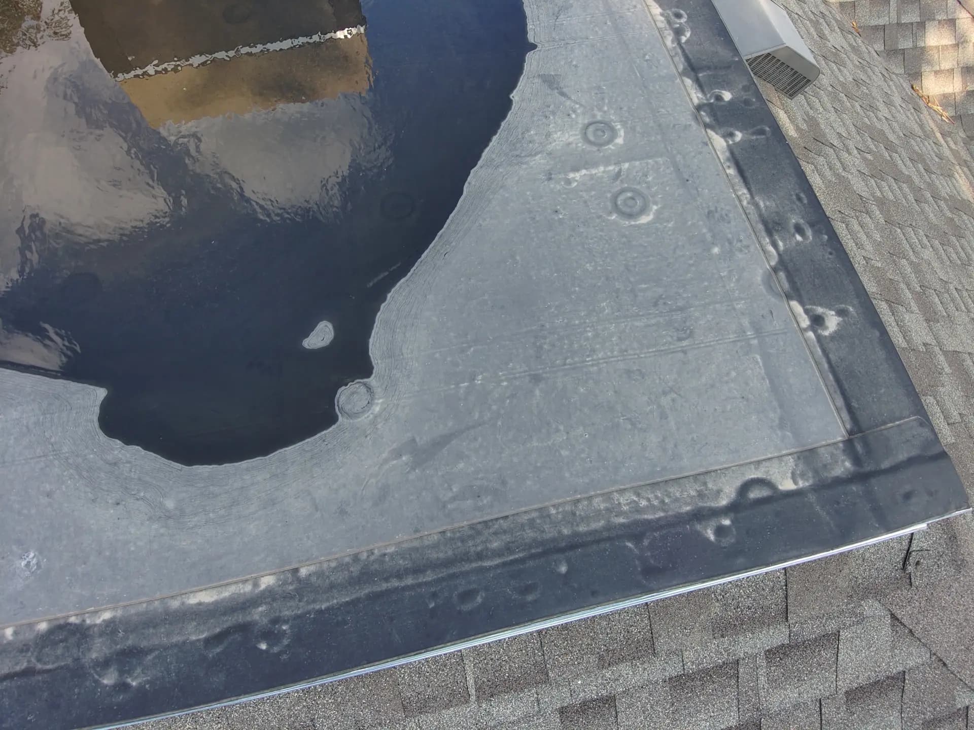 Low-slope roof section on a home in Denver, Colorado showing hail bruising and standing water beside the adjacent shingle roof
