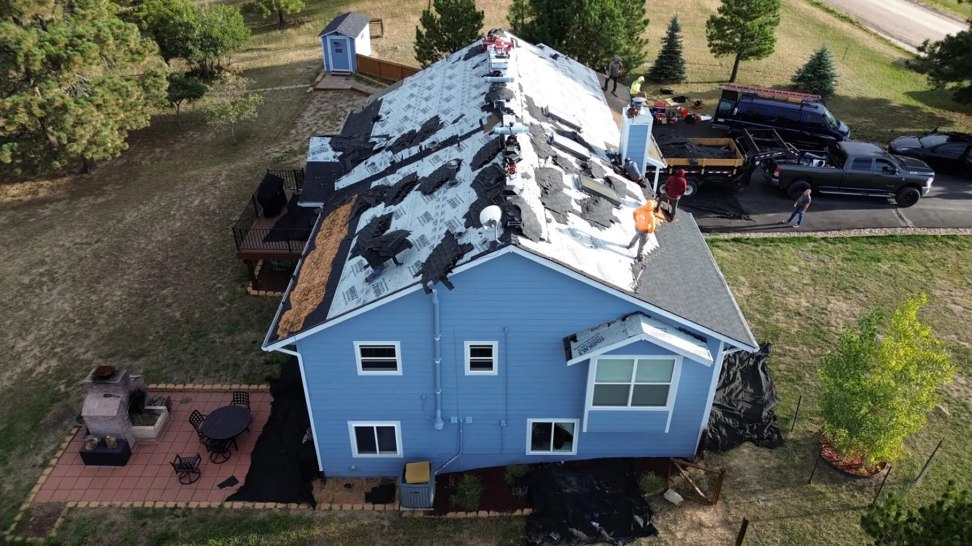Aerial view of a hail-damaged roof being torn off to the underlayment on a two-story home in Elizabeth, Colorado, with the crew and dump trailer on site
