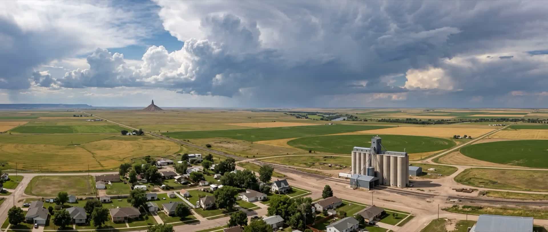 Illustrative representation of a small farming town on the High Plains at Bayard, Nebraska, with grain elevators and irrigated fields under a storm sky