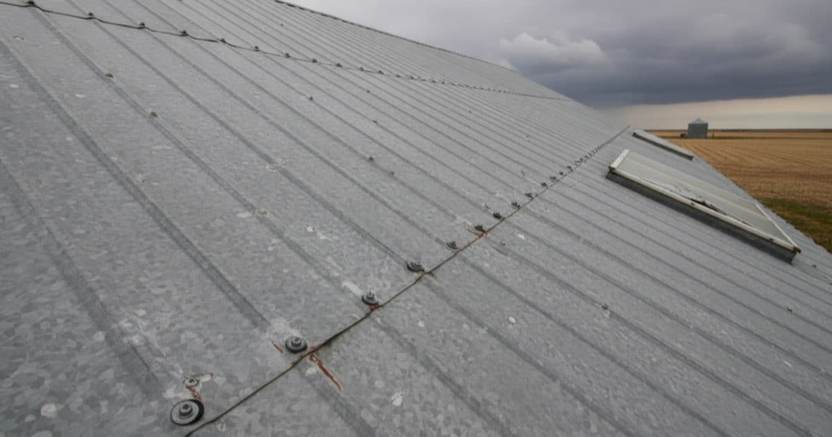Illustrative representation of hail damage on a galvanised steel farm machine shed in western Nebraska: dented panels, split fastener washers, and rust weeping from fractured coating