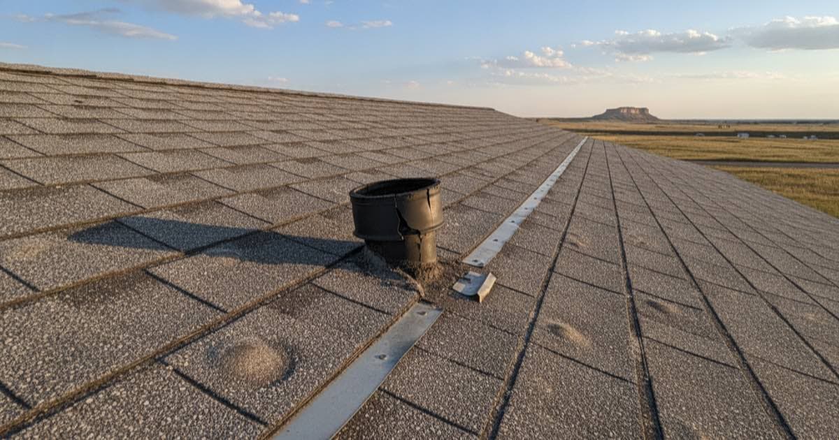 Illustrative representation of a weathered asphalt shingle roof near Scottsbluff, Nebraska with a split rubber pipe boot and lifted step flashing, prairie and a sandstone bluff behind